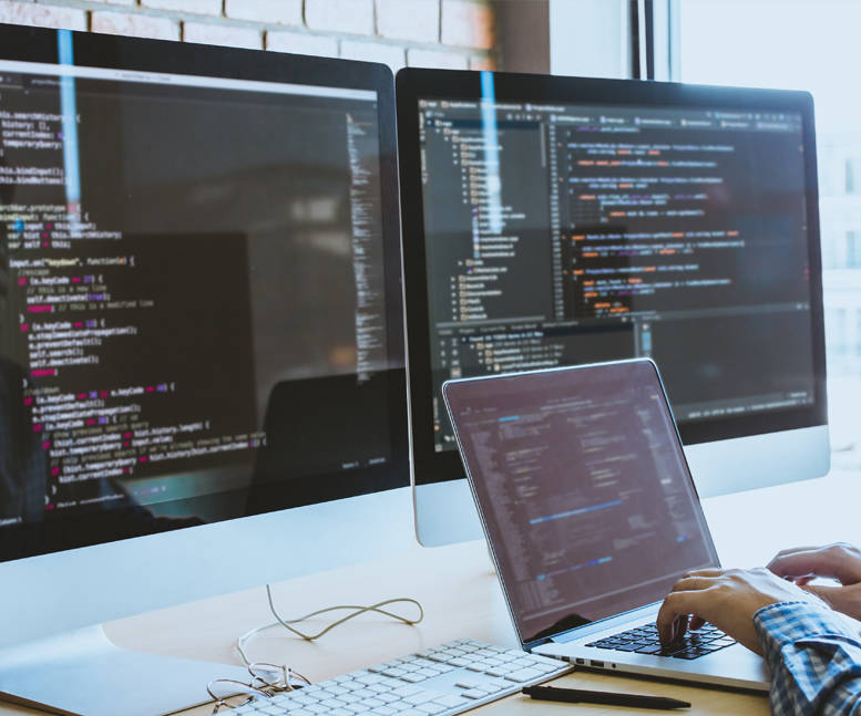 A person using programming software on a laptop with 2 large monitors